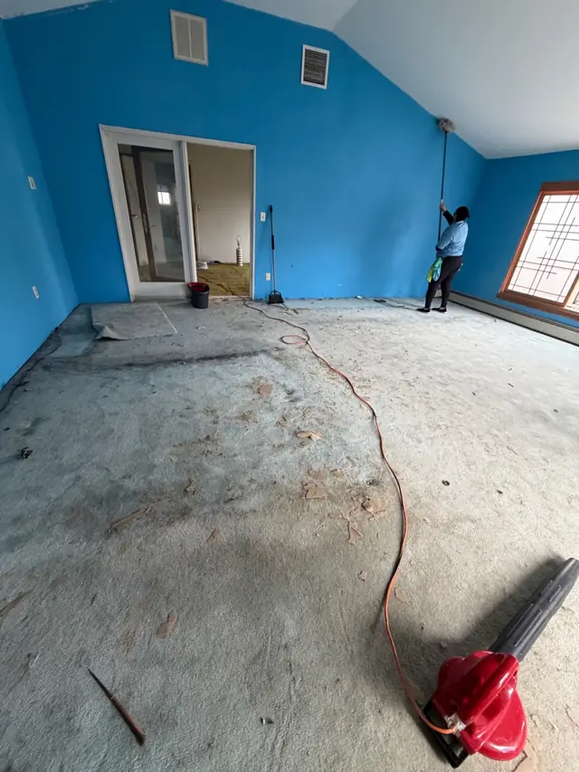 A Dust Buster cleaner dusting the ceiling line of an empty room with bright blue walls
